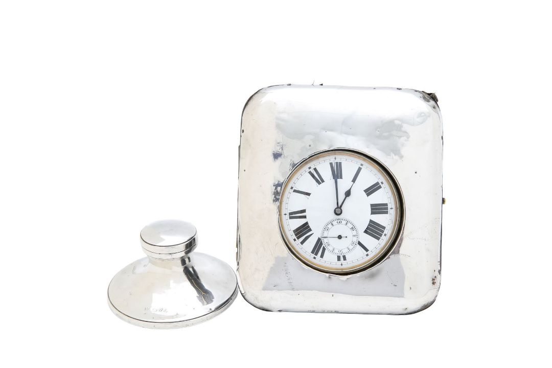 A pocket watch in a silver case and a silver inkwell
