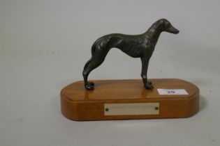A cold cast copper oxidised figure of a racing greyhound, mounted on a wood base, figure 10cm high
