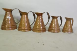 Set of five graduated hammered copper jugs, largest 27cm high