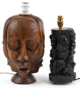 Two African hand figural table lamps, one carved with three faces, the other carved with figures