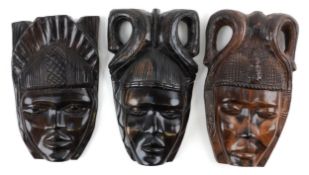 Three hand carved African hardwood wall masks, each with a carved headdress, the largest 34.5cm