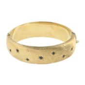 A 1960s textured 9ct gold bangle, with scattered sapphire and engraved stars