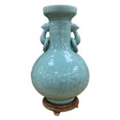 A Chinese celadon glazed vase with twin handles, decorated in low relief, raised on hardwood