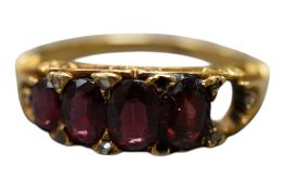 A yellow metal and graduated four stone(ex 5) garnet set half hoop ring, size L/M, gross weight 3.
