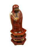 A Japanese pottery figure of Daruma, on an associated Chinese lacquer hexagonal wood stand, height