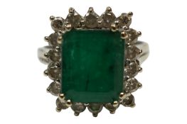 An 18k white metal and single stone emerald rectangular ring, with diamond set border, size O, gross