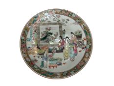 A Japanese porcelain charger, decorated in polychrome enamels with figures in a garden interior,