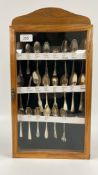 AN OAK DISPLAY CASE CONTAINING A COLLECTION OF 22 VARIOUS SILVER TEASPOONS.