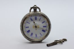 AN ORNATE ANTIQUE SILVER CASED FOB WATCH, ENAMEL DIAL AND KEY.