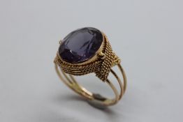 AN UNUSUAL YELLOW METAL AMETHYST DRESS RING, THE OVAL STONE SURROUNDED BY A BEADED BAND MARKED 14.