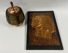 A COPPER EMBOSSED EGYPTIAN PLAQUE ALONG WITH A COPPER FINISH AND ETHNIC DESIGN TABLE LAMP - SOLD AS