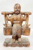 A VINTAGE EASTERN CARVED WOODEN SCULPTURE DEPICTING A BOY CARRYING A YOKE WITH TWO BARRELS /