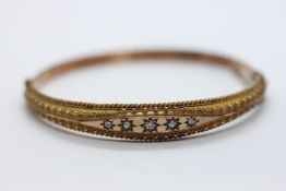 AN ANTIQUE 9CT GOLD HINGED BANGLE SET WITH FIVE SMALL DIAMONDS.