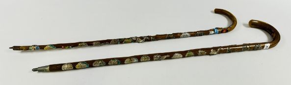 TWO WALKING STICKS ADORNED WITH VARIOUS SOUVENIR BADGES.