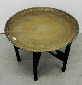 A LARGE VINTAGE PERSIAN ENGRAVED BRASS SERVING TRAY SUPPORTED ON A FOLDING CARVED WOODEN BASE -