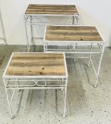 A GRADUATED SET OF THREE ANTIQUE EFFECT METAL CRAFT OCCASIONAL TABLES WITH WOODEN TOPS.