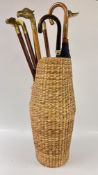 A GROUP OF 6 ASSORTED BRASS HANDLED WALKING STICKS + 3 X UMBRELLAS IN A SEAGRASS STAND.