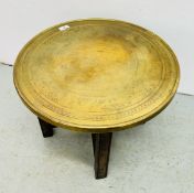 A VINTAGE PERSIAN ENGRAVED CIRCULAR BRASS TABLE TOP SUPPORTED ON A FOLDING WOODEN BASE - DIAM 52CM.