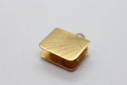 A 9CT GOLD CHARM IN THE FORM OF A BOOK CONTAINING A WHITE STONE.