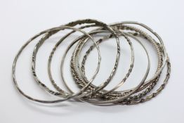 A GROUP OF 8 SILVER AND WHITE METAL BANGLES.