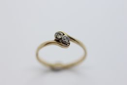 AN UNMARKED YELLOW METAL TWO STONE DIAMOND CROSS OVER RING.