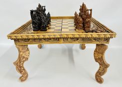 AN ORNATE CARVED WOODEN CHESS TABLE AND PRESS PLUS DRAFTS PIECES 62 X 62CM.