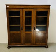 A PLAIN EARLY C20TH LIGHT OAK BOOKCASE WITH TWO PARTIALLY GLAZED DOORS AND CENTRAL PANEL ON BUN