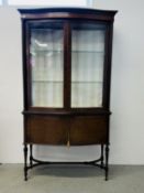 AN EARLY C20TH TWO DOOR DISPLAY CABINET WITH PLAIN SLIGHTLY BOWED DOUBLE DOORS ENCLOSING GLASS