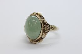 A 9CT GOLD RING SET WITH AN OVAL JADE / HARDSTONE PANEL IN A FLORAL MOUNT.