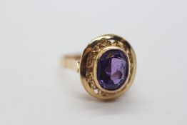 A YELLOW GOLD RING MARKED 18K SET WITH AMETHYST IN RUB OVER SETTING IN A PIERCED OVAL FRAME.