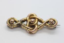 AN EDWARDIAN YELLOW METAL BROOCH OF KNOTTED DESIGN SURMOUNTED WITH THREE BALLS (RUBBED MARKS).