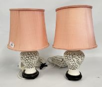 A PAIR OF ORIENTAL PORCELAIN OPEN WORK LAMP BASES WITH PINK SHADES - SOLD AS SEEN.