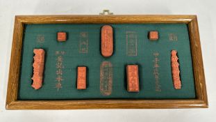 A HARDWOOD FRAMED DISPLAY CONTAINING A COLLECTION OF CARVED WOODEN CHINESE SEALS, W 30 X D 15CM.
