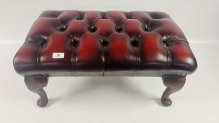 A CHESTERFIELD BUTTON BACK STYLE FOOTSTOOL, UPHOLSTERED IN OXBLOOD RED FAUX LEATHER (TRADE ONLY).