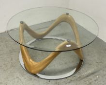 A MODERN DESIGNER CIRCULAR GLASS TOP COFFEE TABLE WITH A CURVED WOODEN BASE.