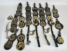 A GROUP OF VINTAGE HORSE BRASSES MOUNTED ON LEATHER STRAPS.