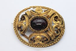 A UNMARKED YELLOW METAL OVAL BROOCH OF SCROLLED DESIGN SET WITH A CENTRAL OVAL PURPLE CABOCHON
