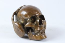 A BRONZE MODEL OF A SKULL WEARING HEADPHONES. 17cms high.
