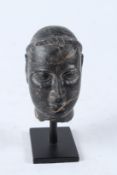 A RARE, POSSIBLY ANCIENT MIDDLE EASTERN, CARVED BLACK STONE HEAD mounted on a stand. 13cms high.