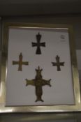 A group of bronze crosses mounted on a framed backing board.