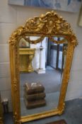 A decorative gilt framed mirror with figural cresting, 158cm x 88cm.