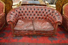 A red leather Chesterfield style two seater settee with curving back.