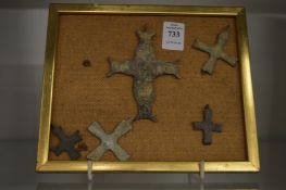 A group of bronze crosses mounted on a framed backing board.