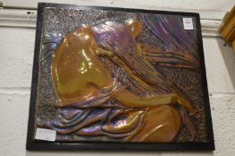 An embossed metal plaque depicting a seated female figure.