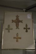 A group of bronze crosses mounted on a framed backing board.