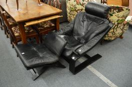 A black leather upholstered cantilever style armchair with matching stool.