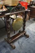 A brass dinner gong suspended on a carved oak frame.