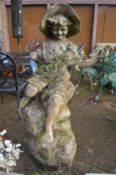 A large reconstituted stone garden ornament modelled as a boy seated on a rock.