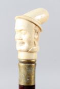 A WALKING STICK with carved bone handle as a man wearing a hat. 92cms long.