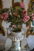 A faux stone pedestal urn containing artificial roses.